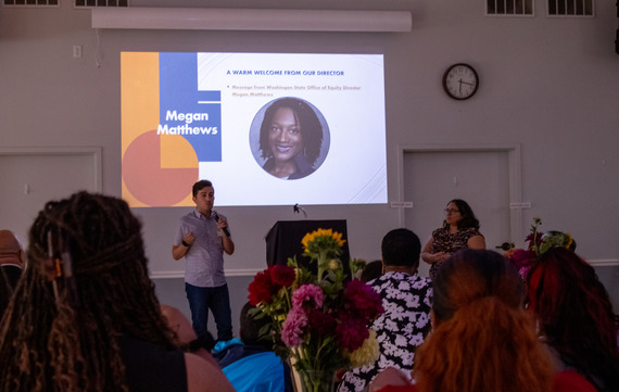 Two people stand in front of a room of seated folks presenting. 