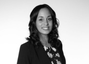 Jasmine is wearing a black suit jacket with a floral print blouse. She is a bi-racial woman, Lithuanian/German and African American.