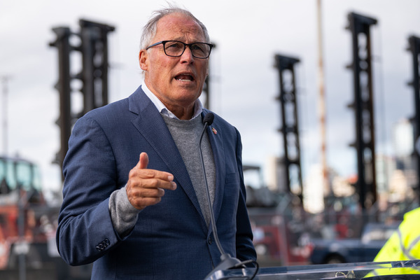 Gov. Jay Inslee speaks with large cranes in the background.