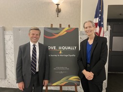 Senator Pedersen and Marsha Botzer smiling in front of Love Equally Poster