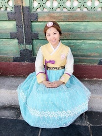 Photo of Stella Chau wearing a traditional Korean hanbok dress with a blue skirt and yellow and white top.