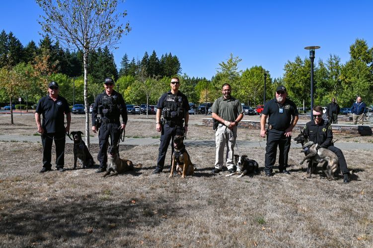 Five narcotics dogs pose with their handlers at a DOC graduation ceremony.