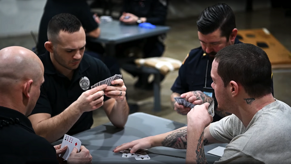 A group of incarcerated individuals plays cards at a table.