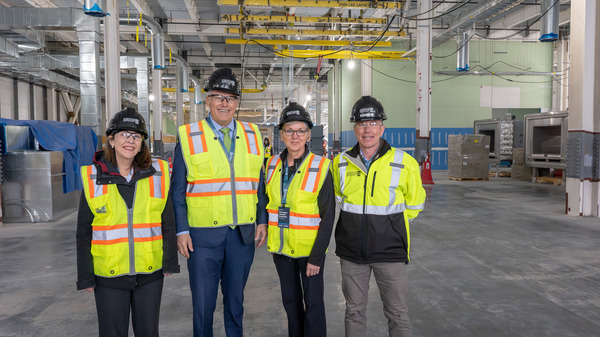 The governor and legislators smile for a picture wearing reflective safety gear in a large warehouse under construction.