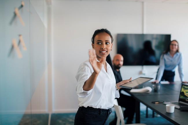 Woman speaking to a group while standing at a dry erase board 