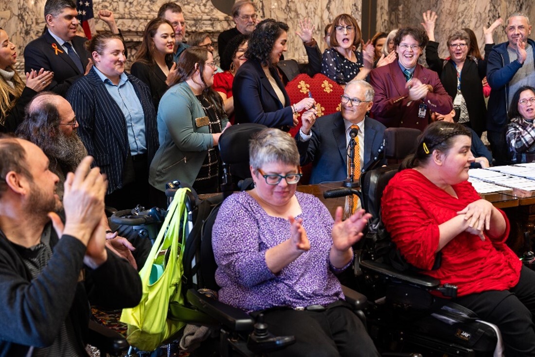 Gov. Jay Inslee signs a bill surrounded by people clapping