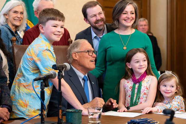 Gov. Jay Inslee signs a bill surrounded by kids.