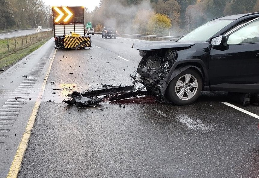 An accident scene after a black vehicle struck a brightly lit "attenuator" vehicle.