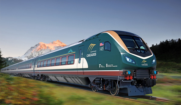 A new diesel-electric Amtrak Cascades train runs with a mountain in the background.