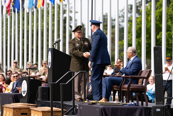 Two generals shake hands onstage at a military event.