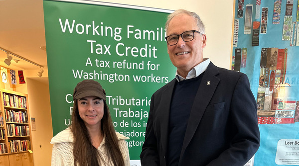 Gov. Inslee standing next to a woman wearing a hat in front of a sign about the working families tax credit