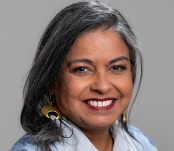 Naghmana Sherazi, a South Asian adult with black and gray hair and brown skin, wearing gold earrings and a buttoned blue shirt with beaded details