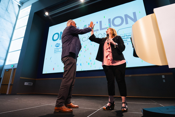 Gov. Jay Inslee high-fives ESD Commissioner Cami Feek on a stage with a projected message "one million Paid Leave" applications displayed behind them.