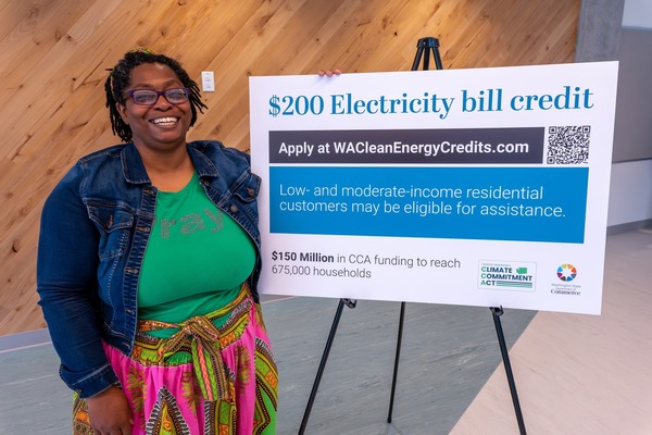 A woman smiles and poses by a sign advertising a new $200 utility bill credit program.