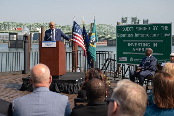 A man speaks at a podium with the I-5 Interstate Bridge in the background.