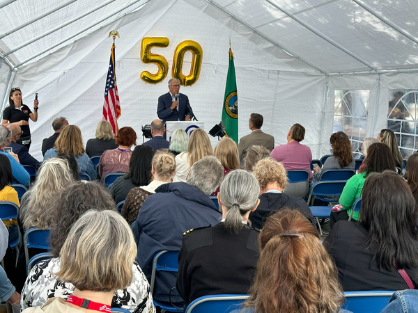 Gov. Inslee speaks from small stage adorned with balloons that say 50