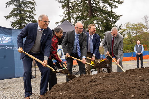 A group of legislators in suits uses ceremonial shovels to dig into a dirt pile.