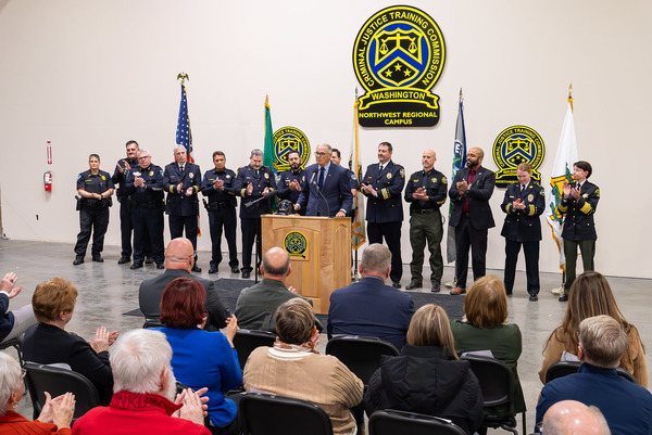 A line of police officers stand behind Gov. Jay Inslee as he speaks at a podium at the opening of a police training center.