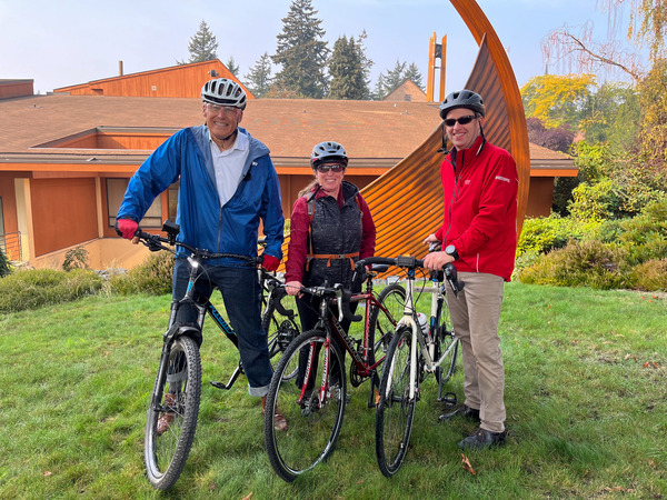 Three people with bicycles smile for a photo.