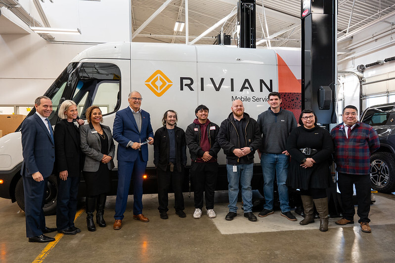 A of auto technicians smiles for a photo in front of a Rivian repair truck.