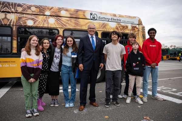 A group of kids smiles with the governor next to an electric bus