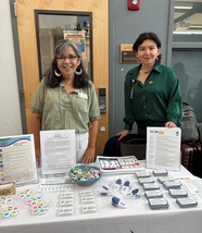 Two people pose and smile behind a table filled with resources, candy, and fidget toys.