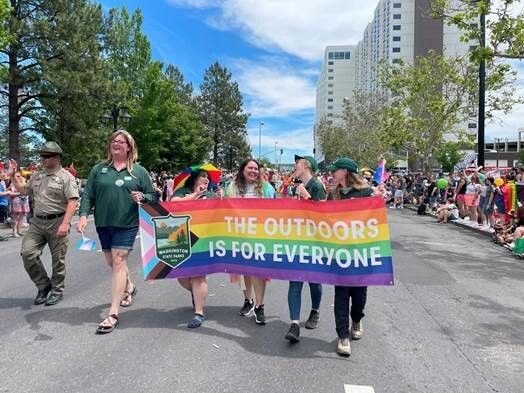 Washington State Parks employees marching with rainbow banner reading "the outdoors is for everyone"
