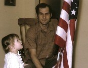 Heidi Helsley as a child standing next to her father looking at an American flag