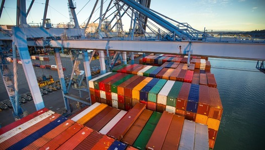 An elevated view of a container ship at a port, loaded with colorful cargo containers. 