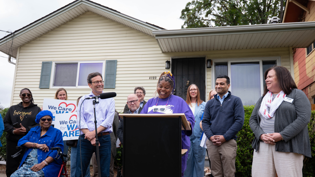 Home care aide Sonja alongside Gov Ferguson and others outside of Evelyn's home