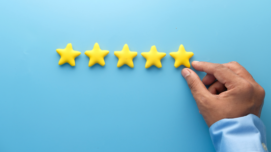 Photo of a person's hand placing the final yellow star to complete a horizontal row of five stars representing a top rating or review.