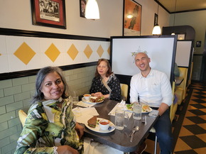 Three people sit at a table in a diner smiling at the camera
