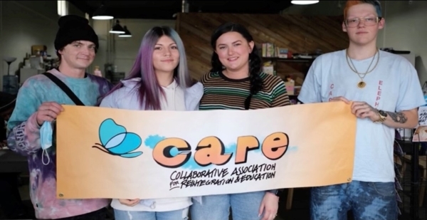 Four people holding a "Collaborative Association for Reintegration and Education (CARE)" banner