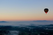 A hot air balloon flies over a foggy mountain at sunset