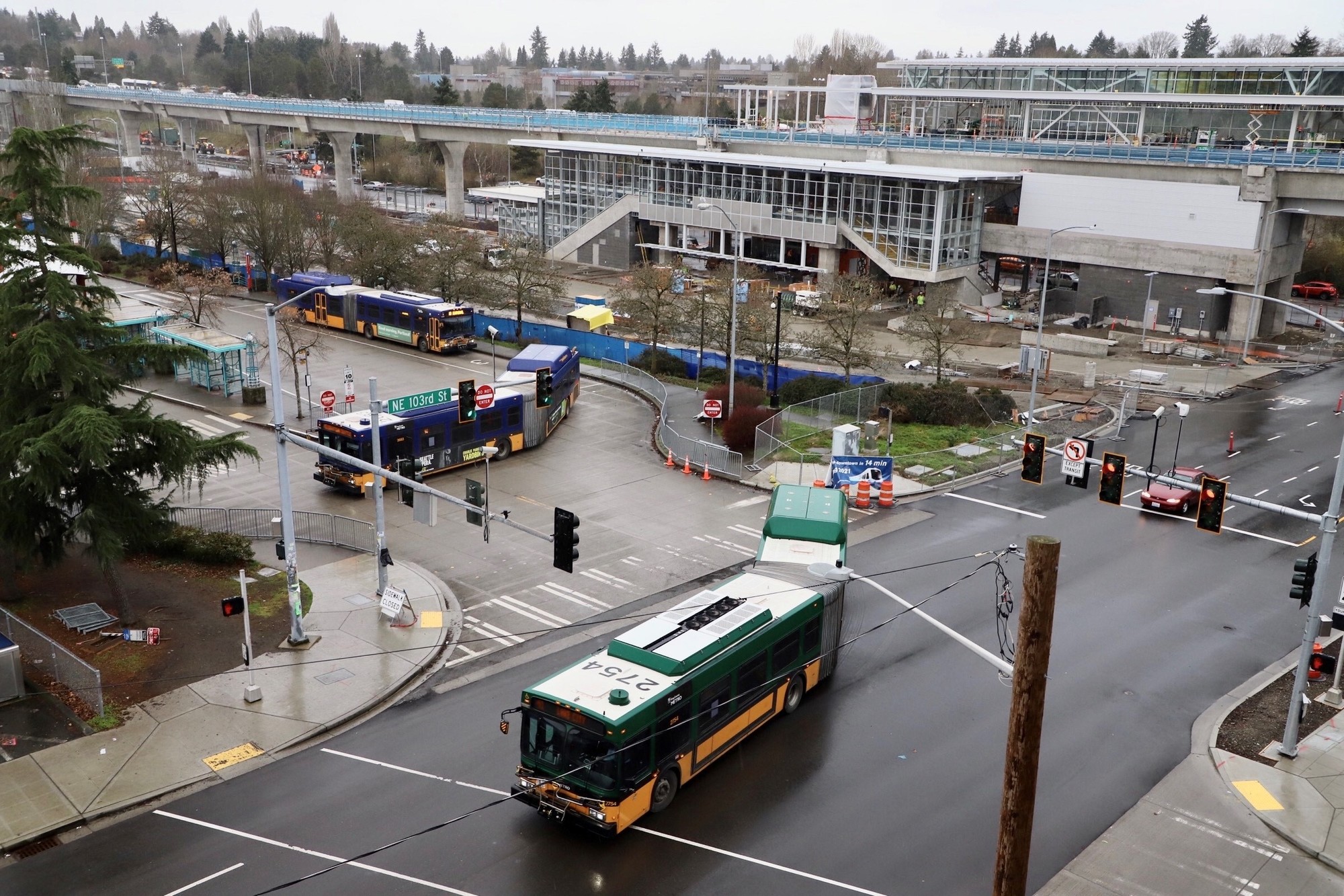 Photo of Northgate Link light rail station taken from NE 103rd Street.. There are a couple of Metro buses visible near the light rail station. 