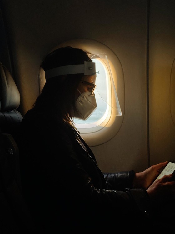 Photo by Camila Perez on Unsplash -Woman on plane wearing mask and face shield 