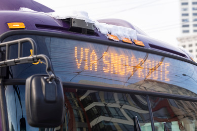 Picture of a Metro bus with snow on top of it and "Via Snow Route" on the destination board