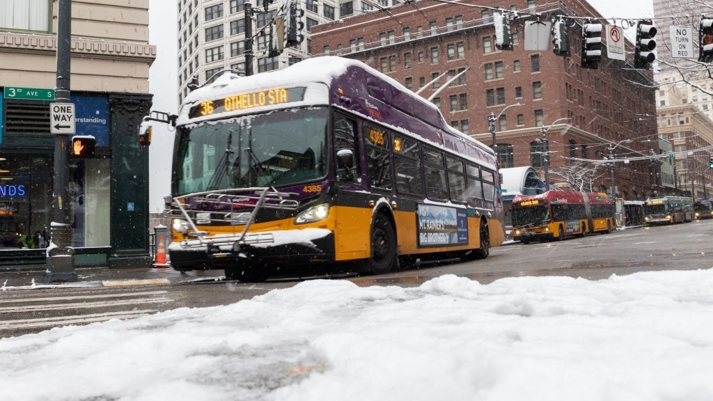 Picture of snow covered buses driving down 3rd Ave. You can see Route 36 and a RapidRide 