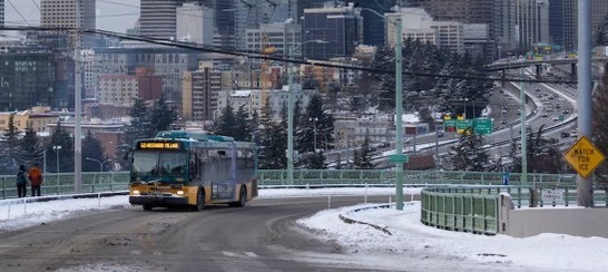 Metro bus driving with the Seattle skyline in the background with a mostly clear road and some snow on the side of the road