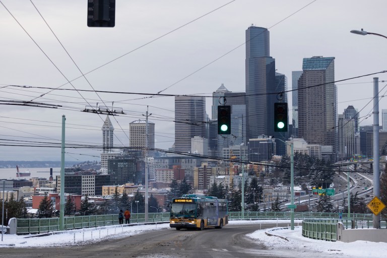 Metro bus driving with the Seattle skyline in the background with a mostly clear road and some snow on the side of the road