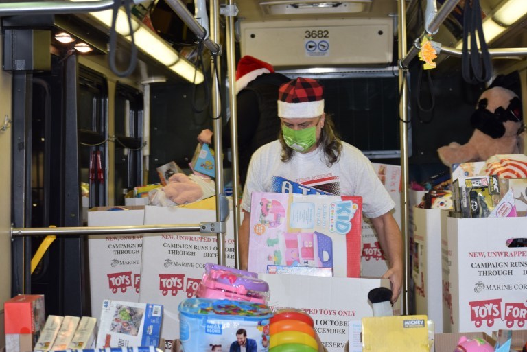 Inside of Metro bus filled with toys for Toys for Tots. Two people in the bus wearing Santa hats as they move the toys. 