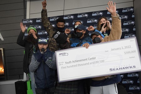 CM Zahilay, the D2 team, and community activists pose with a check for $500,000 from the Seahawks for the Youth Achievement Center 