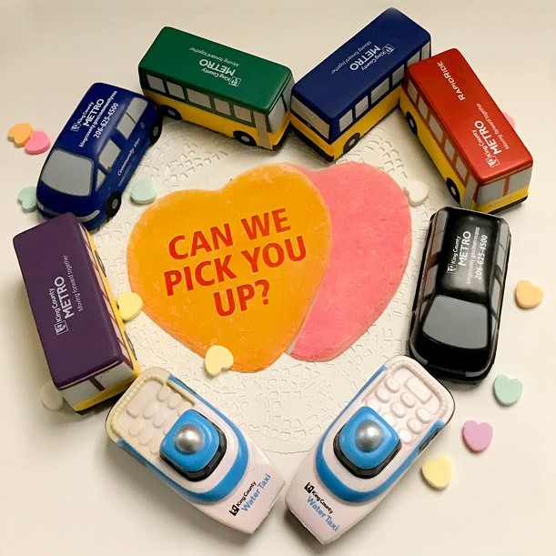 Metro's foam toy buses, vanpool cars, and water taxi boats form a heart. In the middle are two paper hearts that says, "Can we pick you up?"