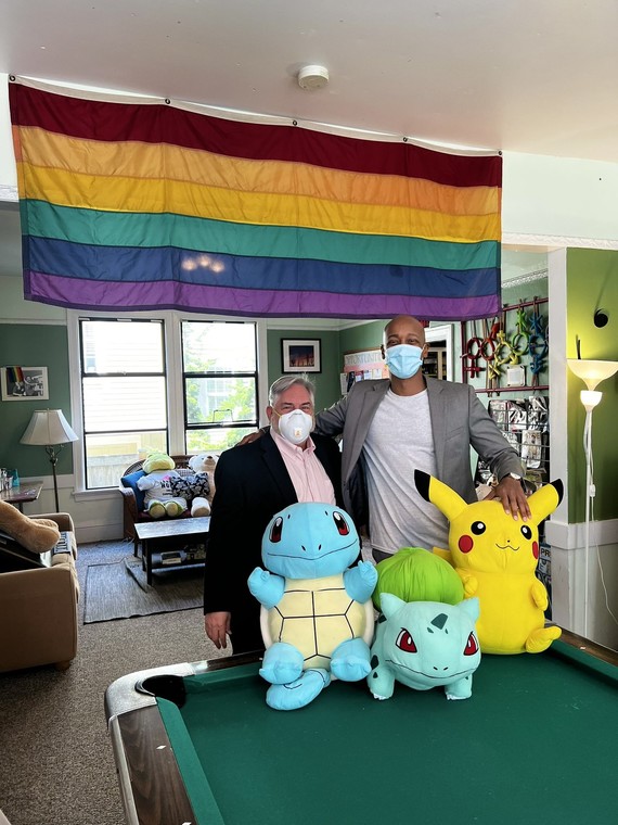 CM Zahilay with a director at the Lambert House, standing behind large pokemon plushies; a pride background is in the background. 