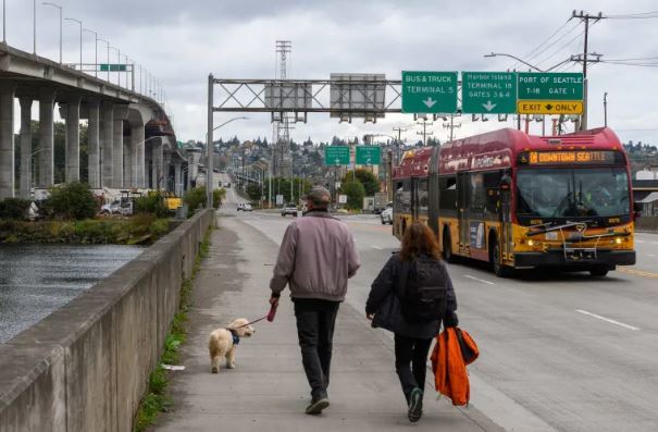 Picture of two people walking on the West Seattle Bridge and C Line bus
