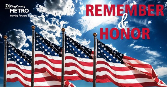 4US flags on tall flag poles are waving in the breeze against a  partially cloudy sky. The text reads "Remember and Honor".