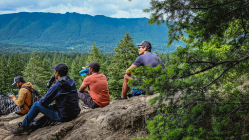 Hikers sit on a mountain sipping water and enjoying the view.