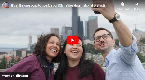 Screenshot of a video that has 3young adults taking a selfie with the Seattle city  behind them and title "It's still a great day to ride Metro!"