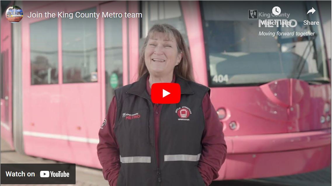 Still shot showing female operator in front of Streetcar from Video titled, "Join the King County Metro team"