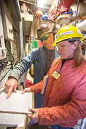 Two people wearing hard hats look at a form in an industrial setting